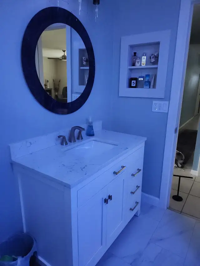 White shaker vanity with marble-look top and a recessed shelf on the wall